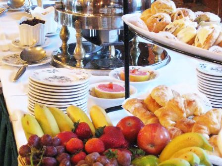 The image shows a buffet table with fruits, pastries, and stacked plates, set elegantly with a decorative serving setup.