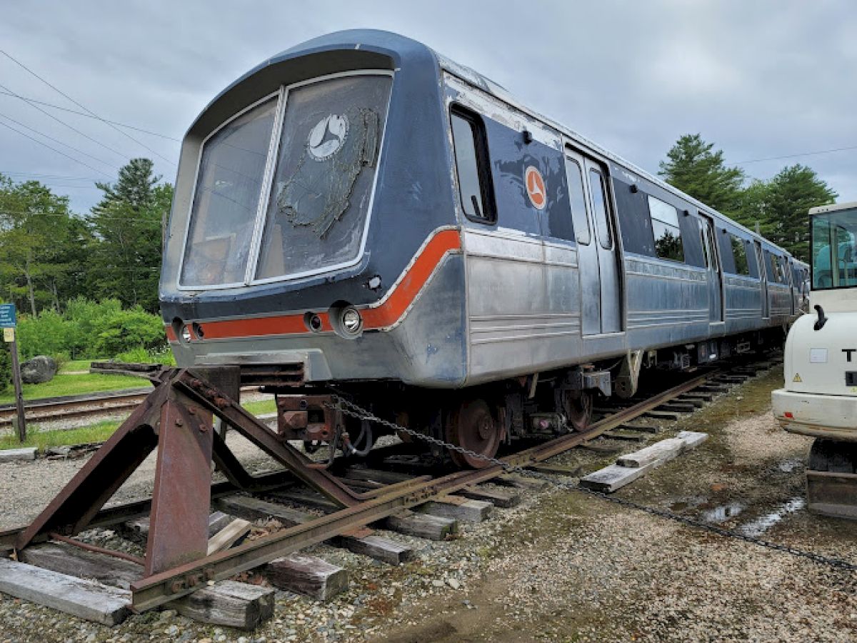 An old, decommissioned subway train on tracks with trees in the background, seemingly part of a storage or display area.