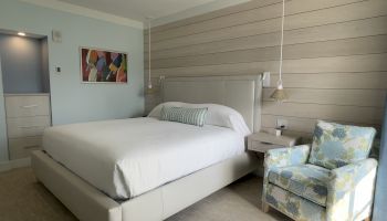 A neatly arranged bedroom with a large bed, decorative pillows, a colorful chair, wall art, and soft lighting.