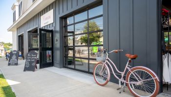A bicycle is parked outside a shop with large windows and chalkboard signs on the sidewalk.