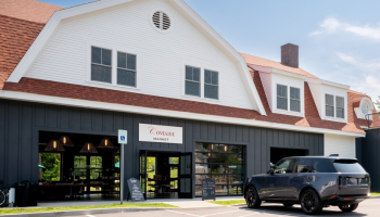 The image shows a building with a red roof and a dark facade. A vehicle is parked in front of it near a sign stating "V Knead."