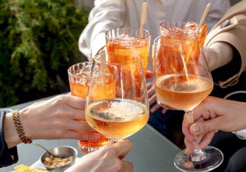 A group toasting with cocktails and wine glasses, clinking drinks outdoors to celebrate together.