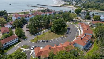 Aerial view of a lakeside coastal resort with red-roof buildings, parking lots, and a wide sandy beach along calm water.