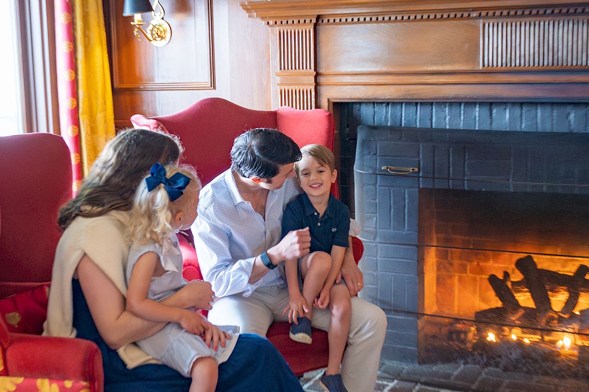 A family sits together by a glowing fireplace in a cozy living room, sharing a warm moment.