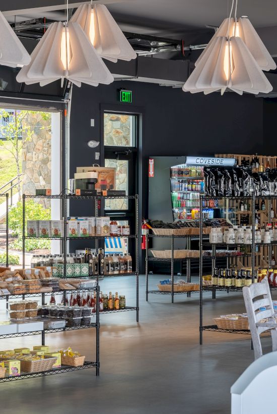 A cozy shop interior with hanging lamps, shelves of coffee and snacks, and a glass case labeled &ldquo;BEVERAGES&rdquo; near the exit.
